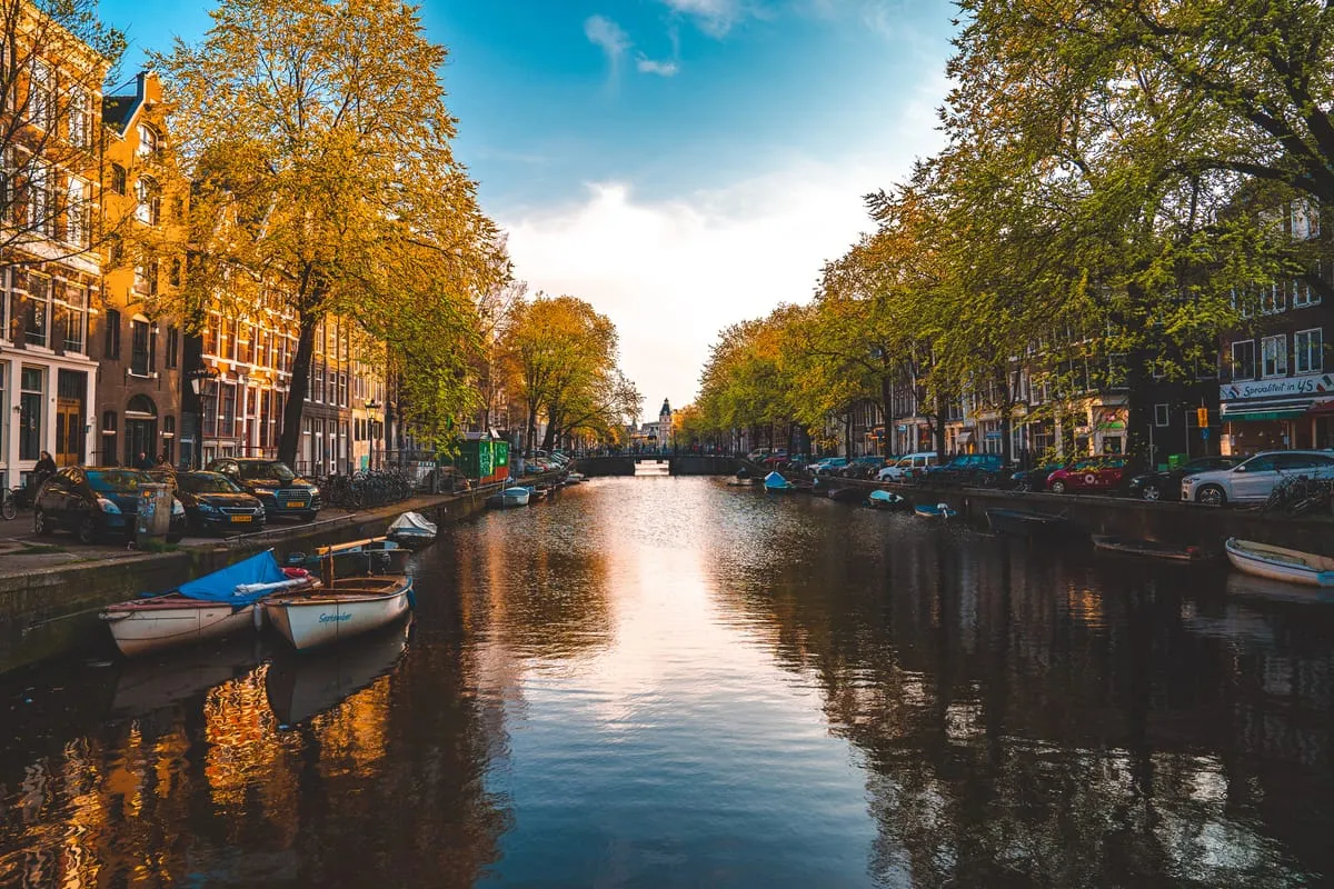 Amsterdam canal at golden hour with moored boats, autumn trees and tall brick canal houses on both banks