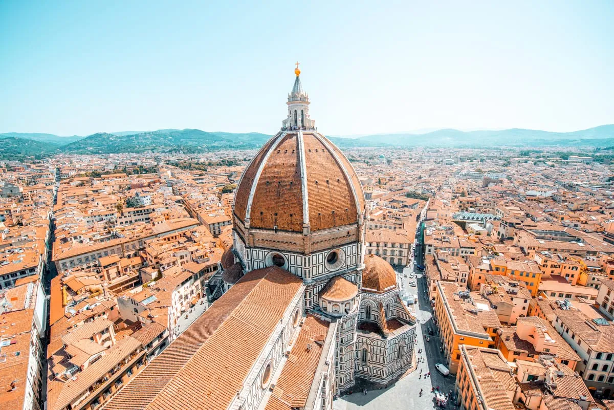 The red-brick dome of Florence Cathedral rising above the terracotta rooftops of Florence, with hills in the distance
