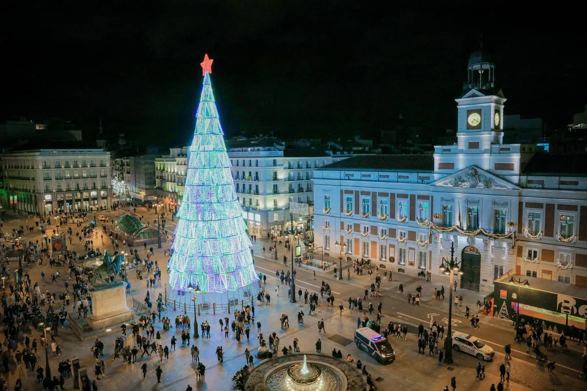 Puerta del Sol in Madrid at night with a tall lit Christmas tree and the clock tower of the Real Casa de Correos