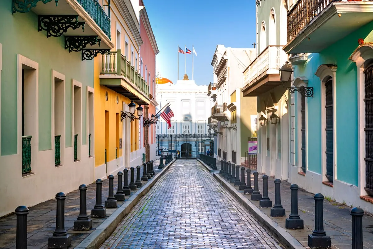 Cobbled street in Old San Juan lined with pastel colonial buildings, iron balconies and American and Puerto Rican flags